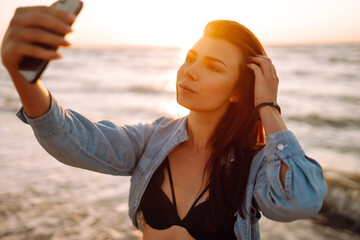 Beautiful girl takes a selfie on the beach at sunset. The concept of relax, travel and summer...