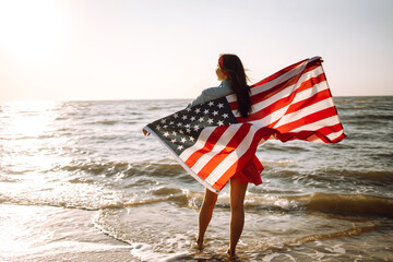 Girl with american flag on the beach at sunset. 4th of July. Independence Day. Patriotic holiday.