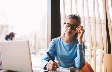 Charming writer in stylish eyeglasses for good vision thinking about creative ideas while recording...
