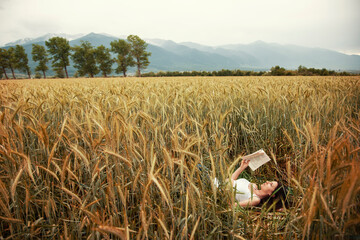 The girl lies in the field and reads a book