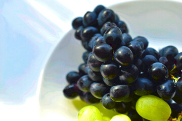 Black and green delicious grapes on a white plate close up