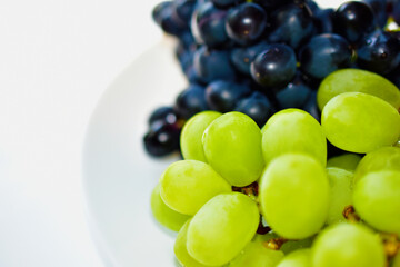 Black and green delicious grapes on a white plate close up