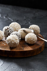 Sweet energy balls with coconut flakes in pile on dark oak slab with silver spon on black background