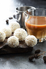 Sweet energy balls with coconut flakes in pile on dark stone with milk phin coffee on black background