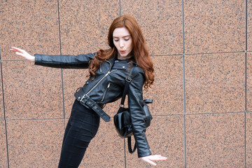 A girl in a leather jacket walks down the street.