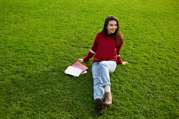Attractive asian student girl relaxing after class sitting with pile of books on beautiful green grass copy space area for text