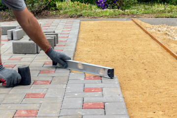 A construction worker installs concrete blocks for sidewalks in the courtyard of a country house.