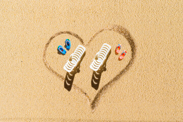 Aerial view of two pair of flip flops, sunbed in shape of heart on sandy tropical beach. Valentines...