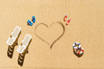 Aerial view of two pair of flip flops, sunbed, lifebuoy in shape of heart on sandy tropical beach....