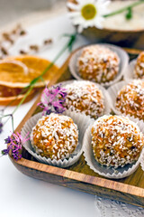  Healthy raw energy balls.Candies vegan balls of dates, coconut pulp, carrots on a wooden tray in paper molds. Top view, concept of useful homemade sugarless candies, coconut energy balls. 