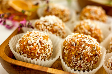  Healthy raw energy balls.Candies vegan balls of dates, coconut pulp, carrots on a wooden tray in paper molds. Top view, concept of useful homemade sugarless candies, coconut energy balls. 