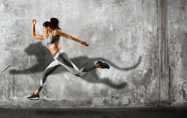 Fototapeta na wymiar Sporty young woman running on wall background