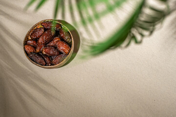 Royal dates fruit in a bowl of coconut on the sand beach under palm branches and leaves shadow.