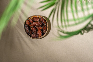 Royal dates fruit in a bowl of coconut on the sand beach under palm branches and leaves shadow.