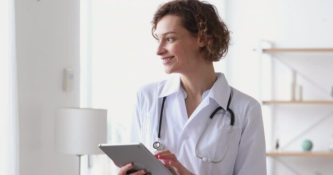 Smiling young female therapist using online healthcare app on digital computer tablet, planning patients appointment in clinic office. Happy doctor general practitioner holding touchpad in hands.