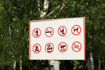 Many prohibition signs on one poster in a summer park. Do not litter, do not smoke, do not drink...
