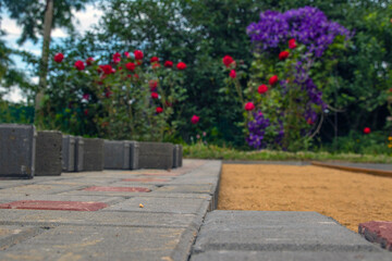 Paving slabs on a sand and gravel basis. Against the background of blooming roses. Selective focus.
