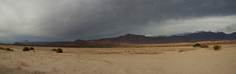 Panorama view of the arid desert. The sand, dunes and mountains under a stormy sky. 