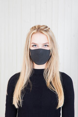 blonde beauty in a black bodysuit and a black protective mask against a white wall