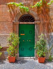Fototapeta na wymiar vintage house exterior with green entrance arched door on ocher wall and flower pots, Trastevere old district, Rome Italy