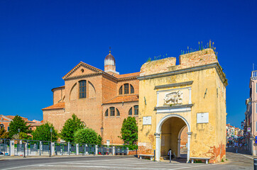 Porta Santa Maria o Porta Garibaldi gate and Cathedral Santa Maria Assunta Duomo catholic church in Chioggia town historical centre, blue sky background in summer day, Veneto Region, Northern Italy
