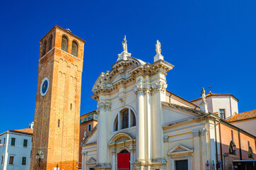 Chiesa Saint Andrea catholic church building with brick bell tower in historical centre of Chioggia town, blue sky background in summer day, Veneto Region, Northern Italy