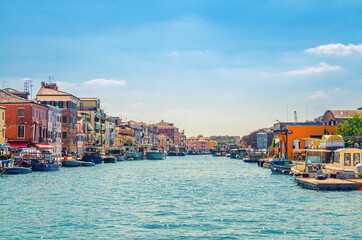 Obraz premium Narrow water canal with moored boats and fishing industrial ships and old buildings on embankment in Chioggia town historical centre, blue sky background in summer day, Veneto Region, Northern Italy