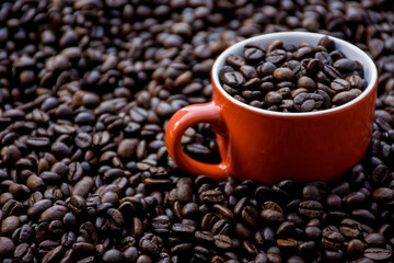 red coffee cup filled and surrounded by black coffee beans