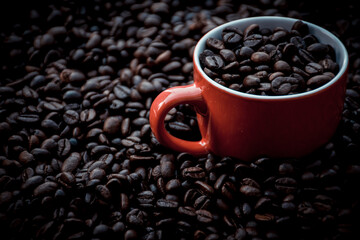 red coffee cup filled and surrounded by black coffee beans