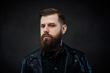 Closeup portrait of a confident stylish bearded man wearing leather jacket in a dark studio