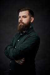Obraz premium Portrait of a bearded young man posing posing with crossed hands and a confident look in dark studio