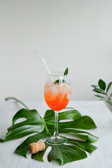 Aperol Spritz cocktail with ice standing on monstera green leaf 