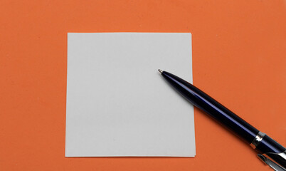 Abstract orange background and white paper with a ballpoint pen, place for text.