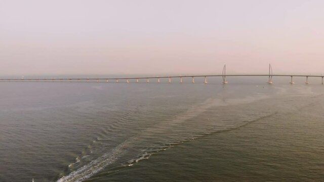 Aerial shot of boat moving away from Hong Kong - Zhuhai - Macau Bridge during golden hour