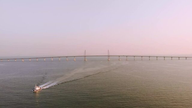 Wide aerial shot of boat moving away from Hong Kong - Zhuhai - Macau Bridge during golden hour