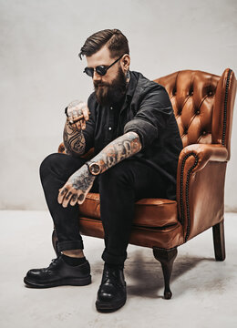 Cool Bearded Young Man Sitting On A Vintage Chair In A White Studio