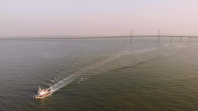 Rising and panning aerial shot of boat with Hong Kong - Zhuhai - Macau Bridge in background during golden hour