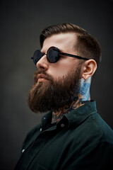 Profile of a young bearded barber with tattoo on his neck in a dark studio