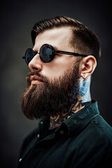Profile of a young bearded barber with tattoo on his neck in a dark studio