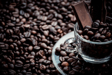 Fototapeta premium Coffee cup with saucer surrounded and filled up with coffee beans and chocolate inside the cup