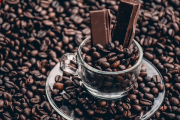 Coffee cup with saucer surrounded and filled up with coffee beans and chocolate inside the cup