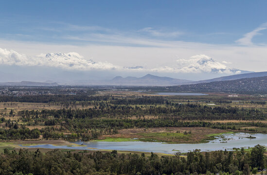 Aerial View Of Mexico City With Ecological Park Xochimilco, One Of Few Remaining Wildlife Habitats In Town, Where Many Migrating Birds Come Every Winter, With Volcanoes Iztaccihuatl And Popocatepetl