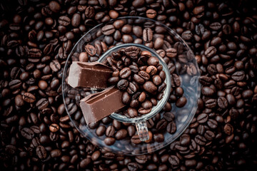 Coffee cup with saucer surrounded and filled up with coffee beans and chocolate inside the cup