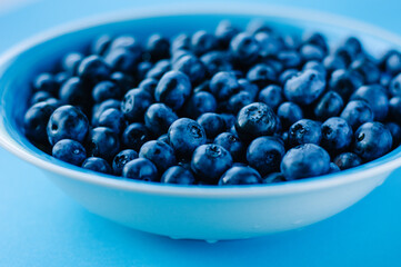 Blueberries in a bowl on a wooden table. Top view of plate and blueberries on violet surface