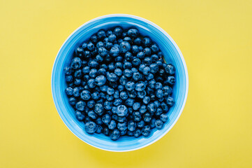 Blueberries in a bowl on a wooden table. Top view of plate and blueberries on violet surface