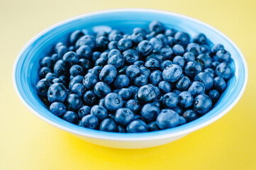Blueberries in a bowl on a wooden table. Top view of plate and blueberries on violet surface