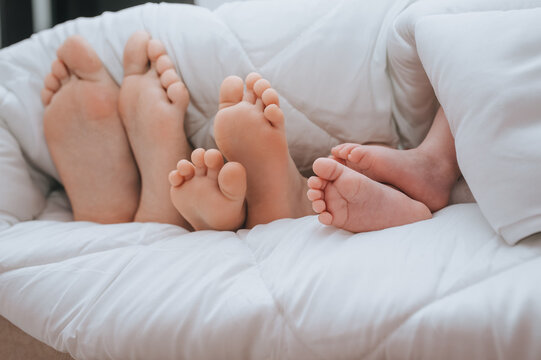 Close-up of the legs of the family of mom, daughter and little newborn son, covered with a plaid. Sleeping family. Time to sleep. Photography, concept.
