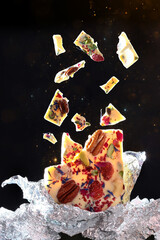 A broken bar of white chocolate. Chocolate with added berries and nuts. Photo on a black background. Copy of the space. The concept of levitation of objects.