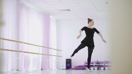 Fototapeta na wymiar A professional ballerina in a black pack dances in a large training hall