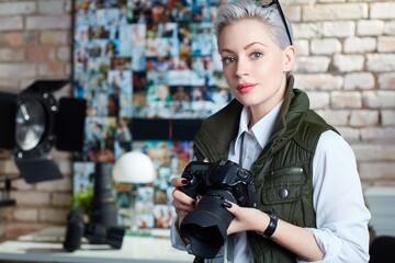 Portrait of attractive young female photographer holding camera, looking at camera. 